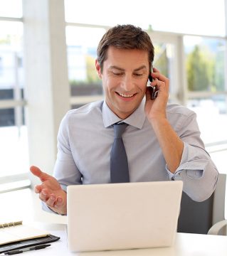 Happy businessman on the phone in front of laptop